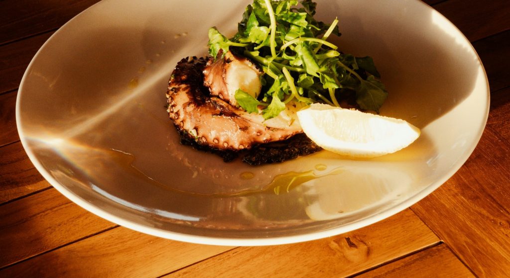 Pulpo a la brasa emplatado con hierbas frescas y limón